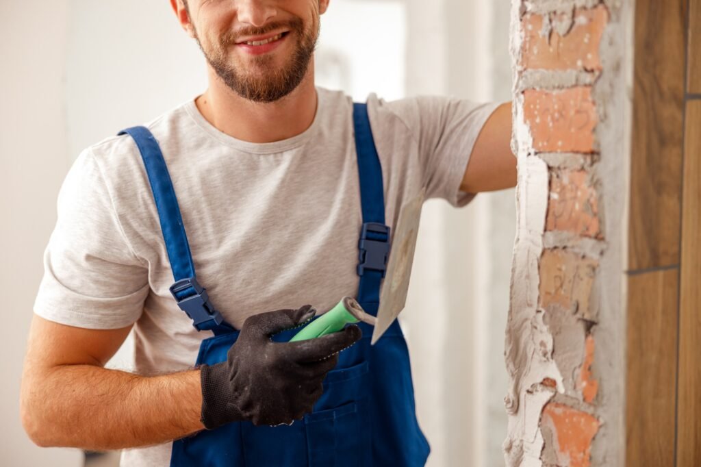 Cropped shot of worker or craftsman using spatula and plastering old cement wall with putty